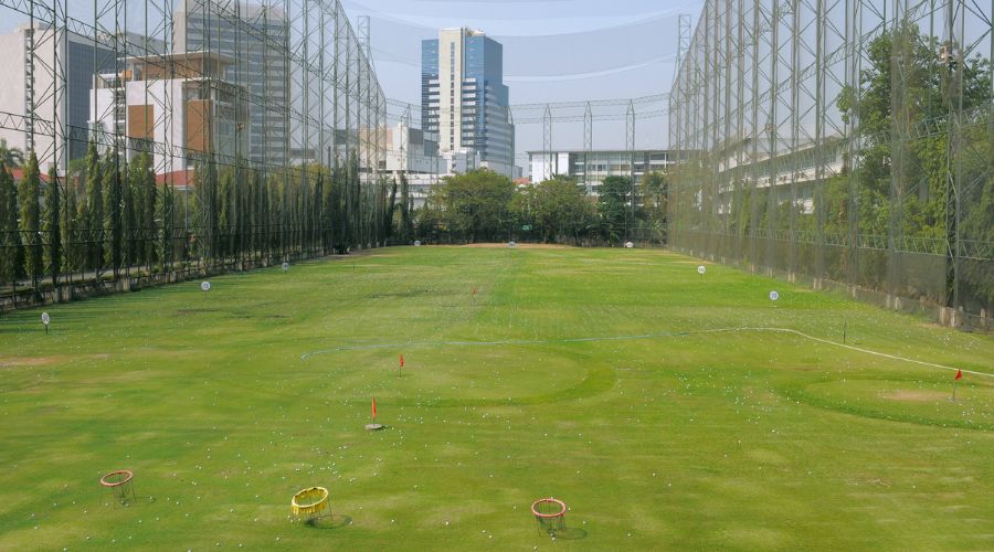 Driving range enclosed by tall netting poles with a city skyline in the background