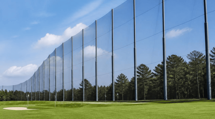 Tall golf range poles supporting safety netting along the edge of a practice area
