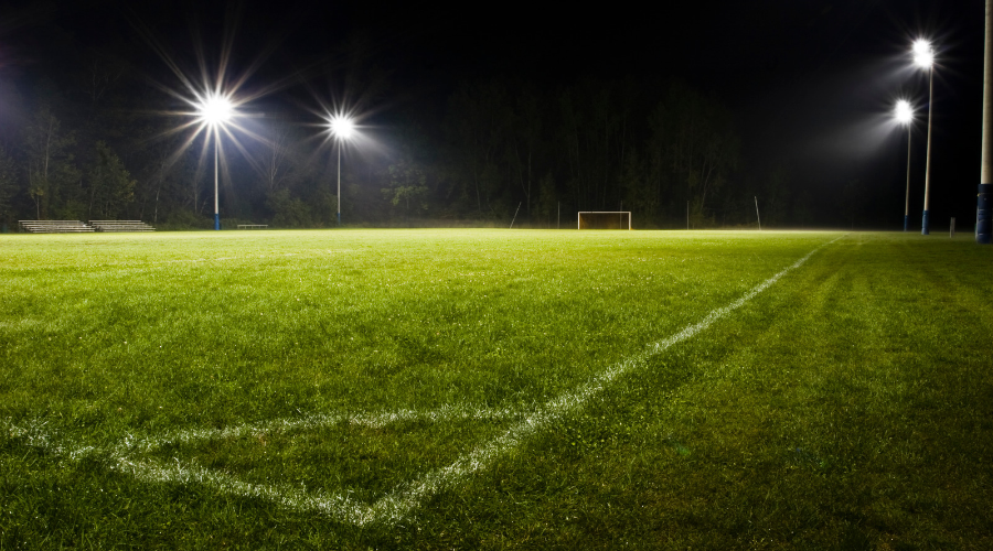 Outdoor soccer field illuminated by pole-mounted floodlights at night.